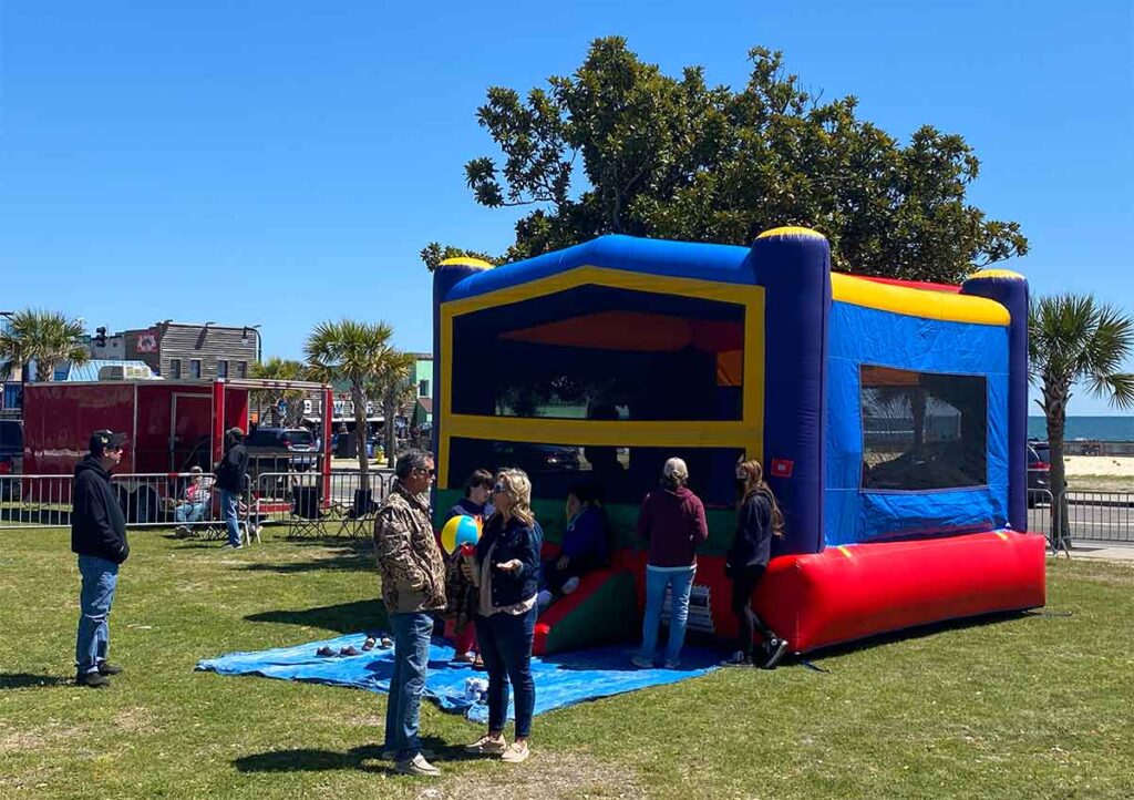 People standing in front of inflatable jump castle as kids play inside at Smoke on the Beach.