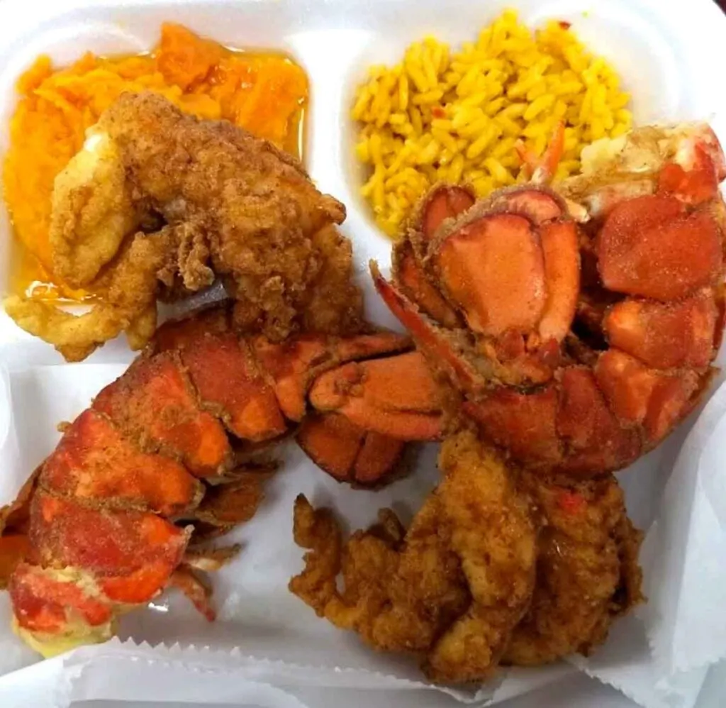 Fried Lobster Tails in styrofoam tray with sides of yellow rice and candied yams.