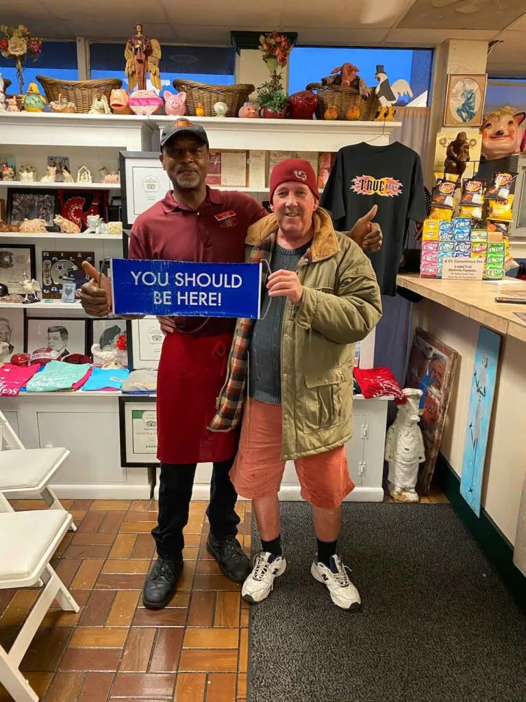 Interior of True BBQ with Milton Zanders and a customer holding a You Should Be Here sign.