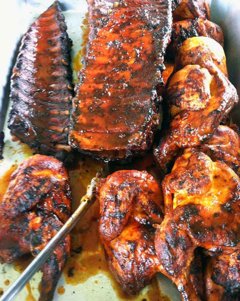 Food bin full of ribs and BBQ chicken, covered in sauce.