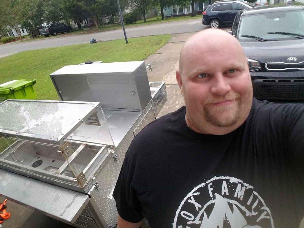 Selfie by Brian Cox with hot dog cart in background in driveway of his home.