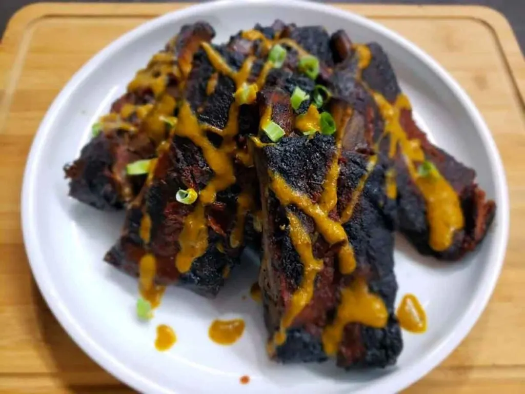 Plate of stacked, individual ribs with mustard sauce and green onion topping