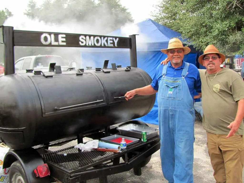 Two BBQ cooks standing beside "Ole Smokey" their BBQ pit.