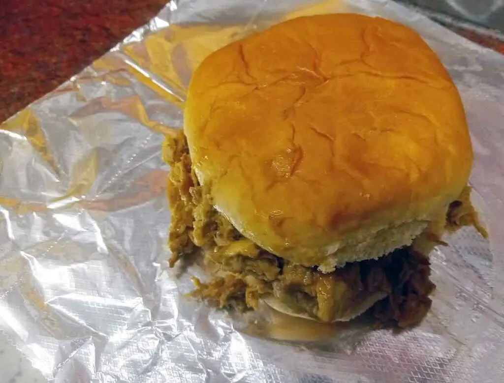 Chopped pork BBQ sandwich on hamburger bun sitting on foil.