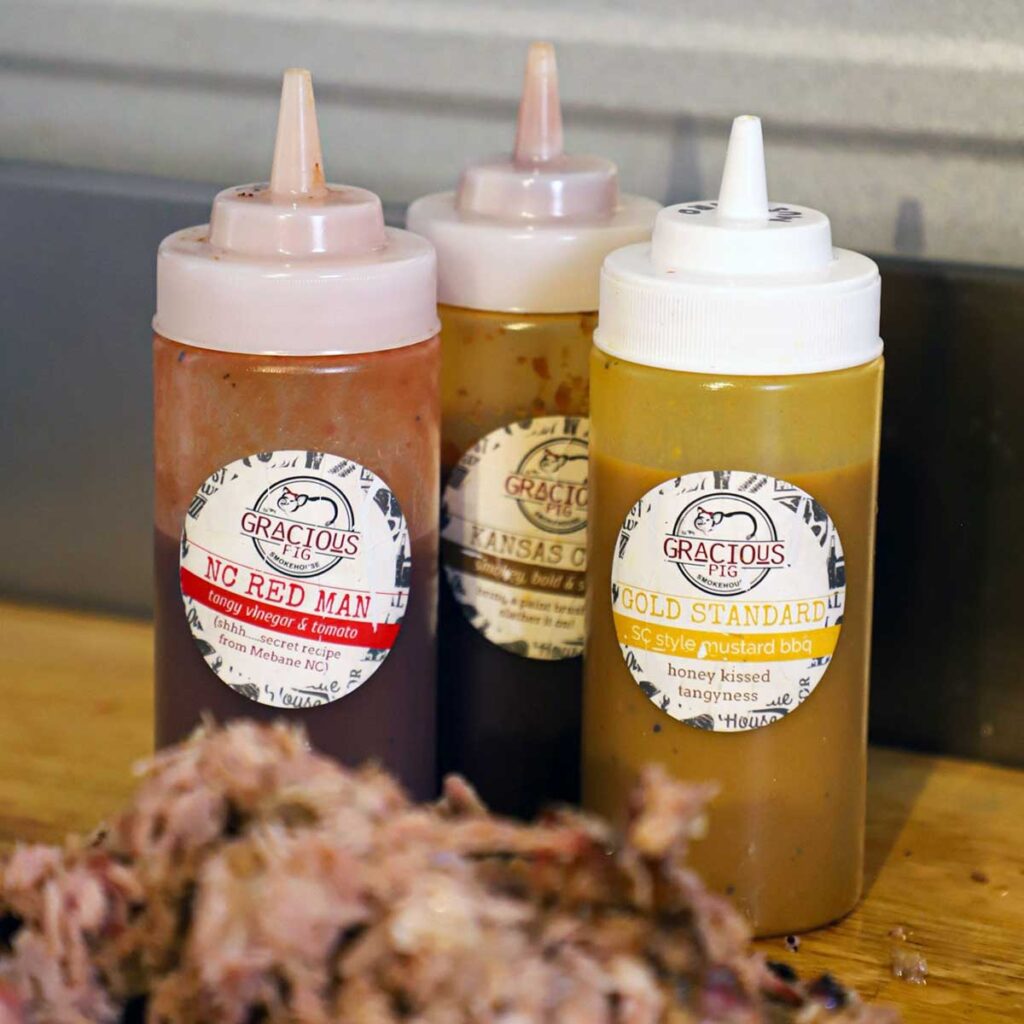 Sauces on table behind a pile of pulled pork.