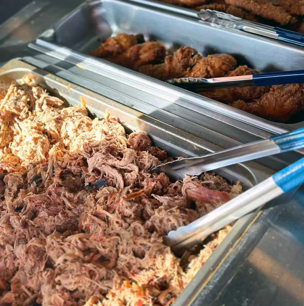 Pan of pulled pork barbecue in buffet tray with tongs.