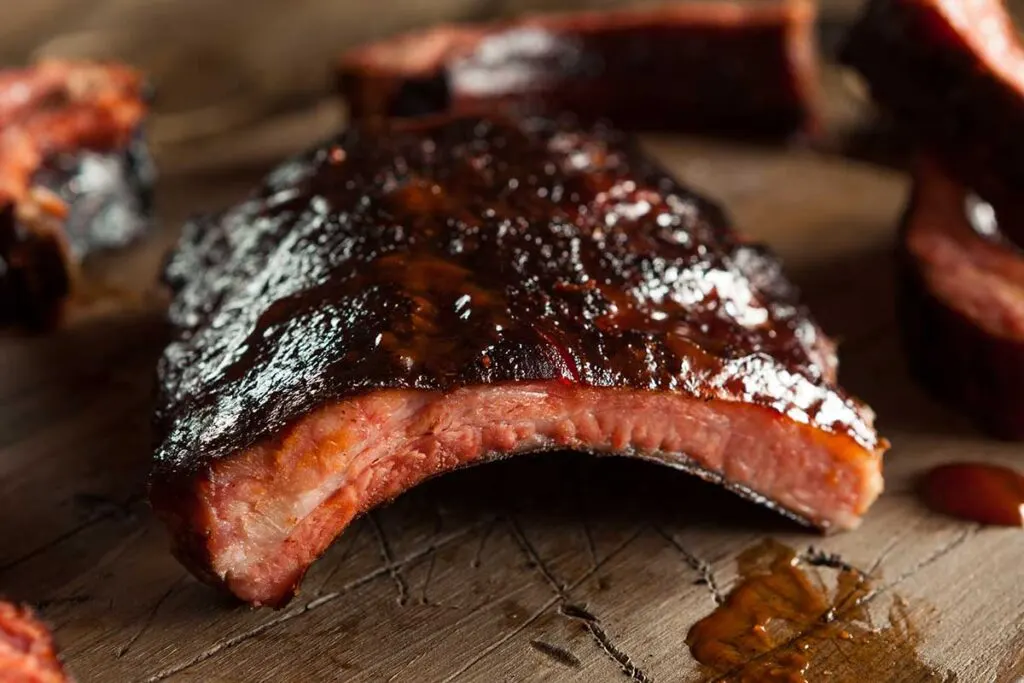 Looking lengthwise down the side of a rack of barbecued baby back ribs, can see the contour of the ribs.