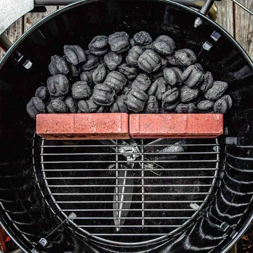 Charcoal briquettes banked behind firebricks on a Weber kettle, creating a clean two-zone grilling setup for indirect cooking.