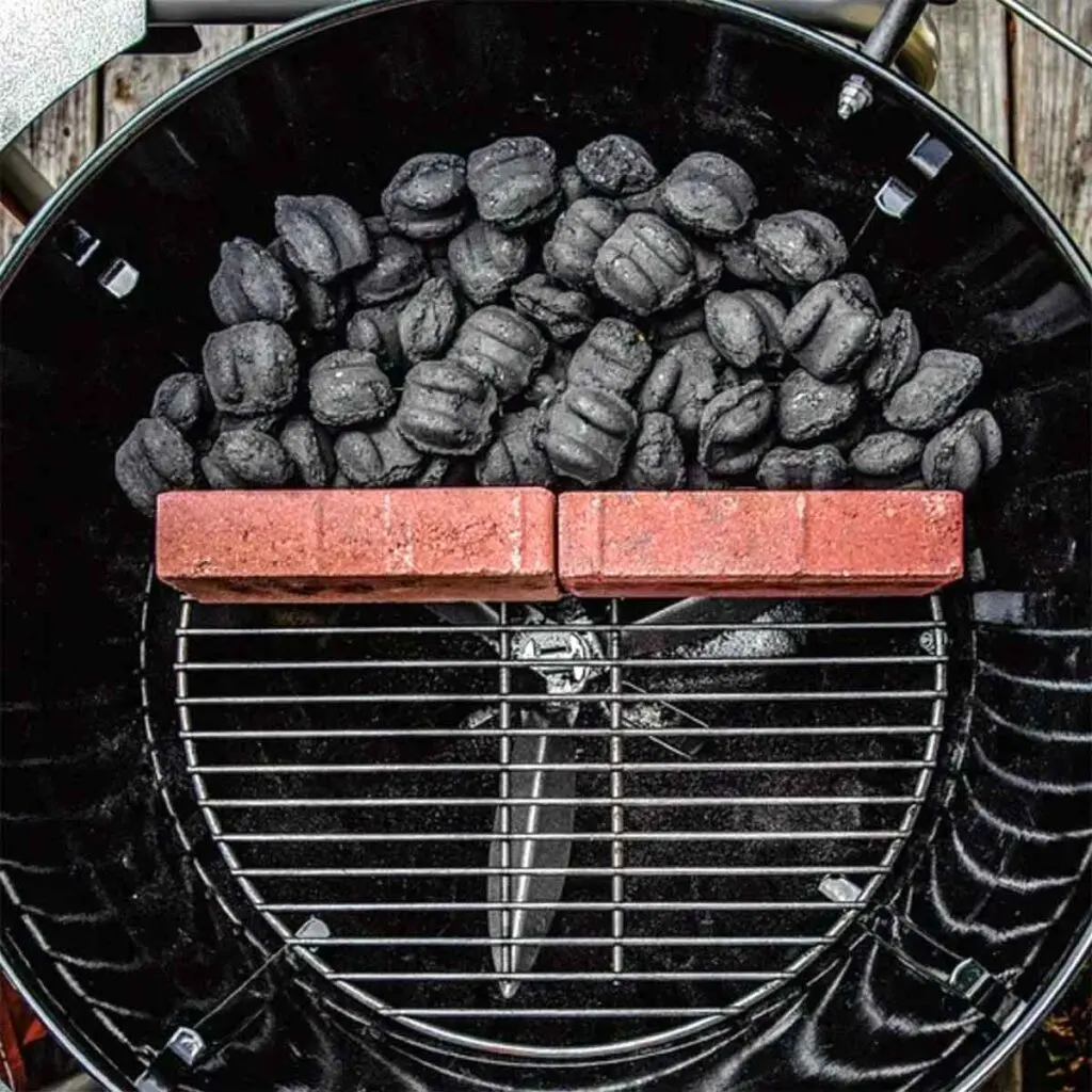 Charcoal briquettes banked behind firebricks on a Weber kettle, creating a clean two-zone grilling setup for indirect cooking.