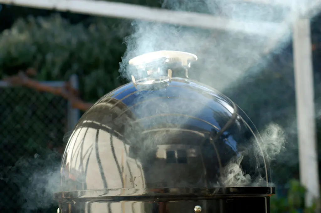 Thin blue smoke surrounding top of smoker.