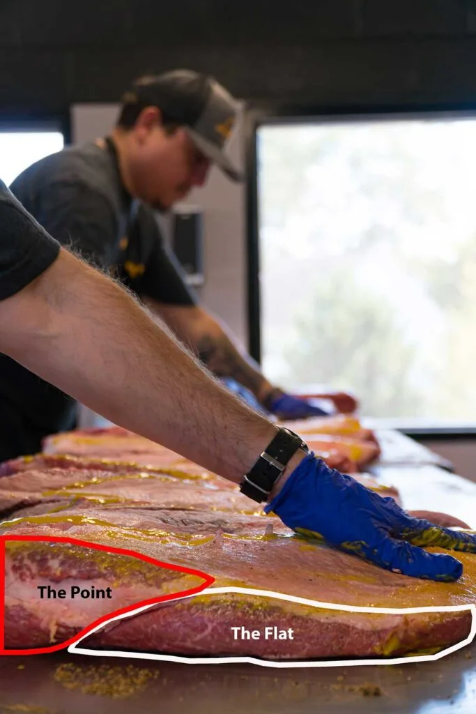 Lewis BBQ workers apply mustard to briskets. Overlay on photo identifies the point and flat of the foremost slab.