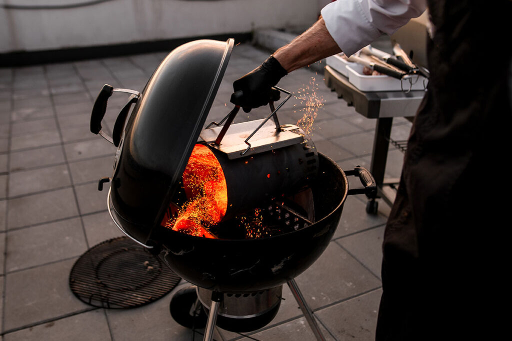 Man pouring hot charcoal into a Webber kettle style grill.