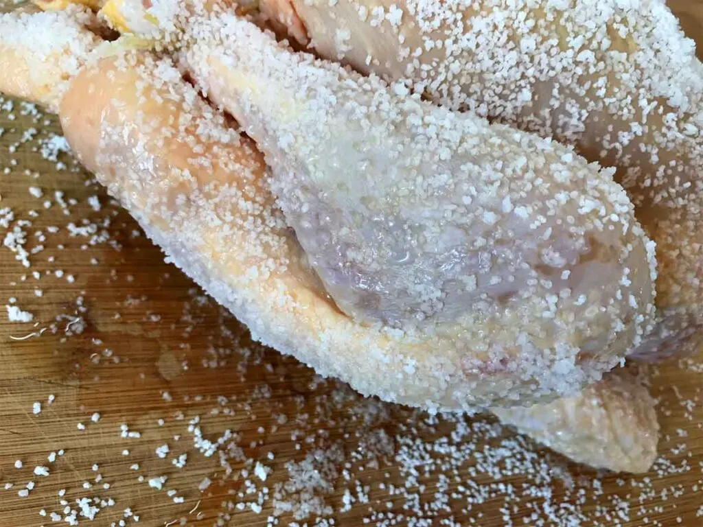 Salt covering raw chicken for dry brining. 
