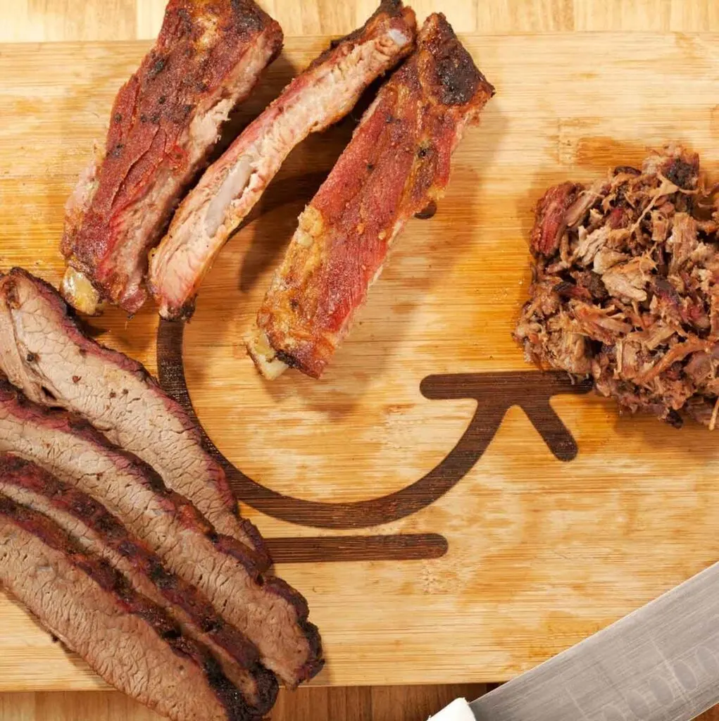 Brisket slices, ribs, and chopped pork BBQ on wooden cutting board with G Brand logo.