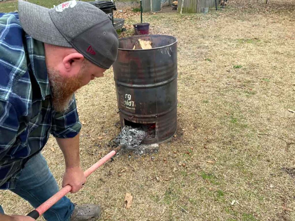 Keith DuBose shovels embers from the bottom of his barrel.