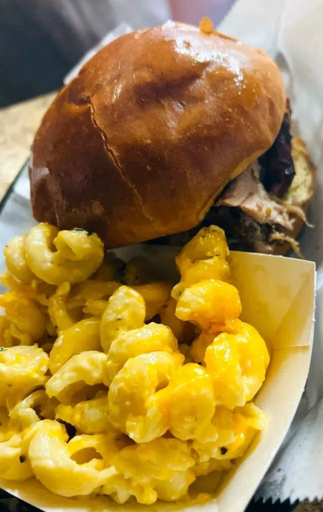 BBQ sandwich in tray with paper container of yellow Mac and cheese.