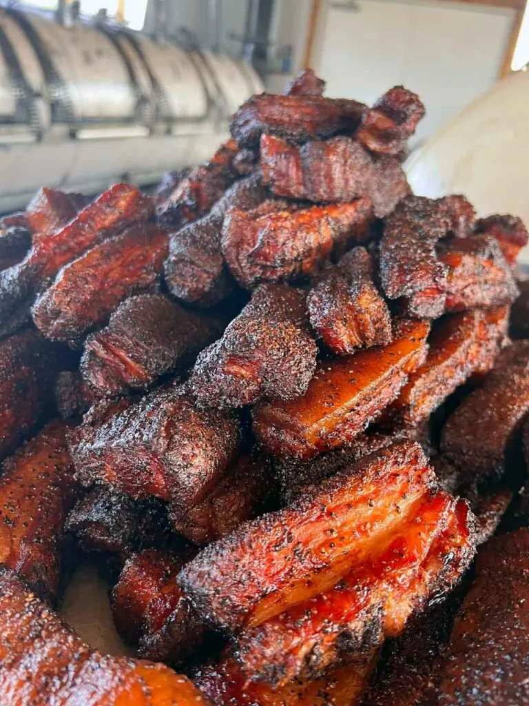Pile of burnt ends with large smoker in background.