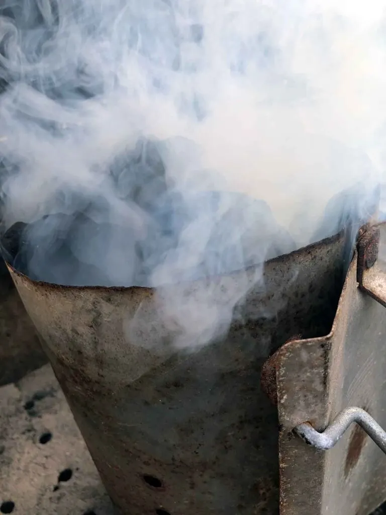 Closeup of the top of a charcoal chimney fire starter with lots of white smoke.