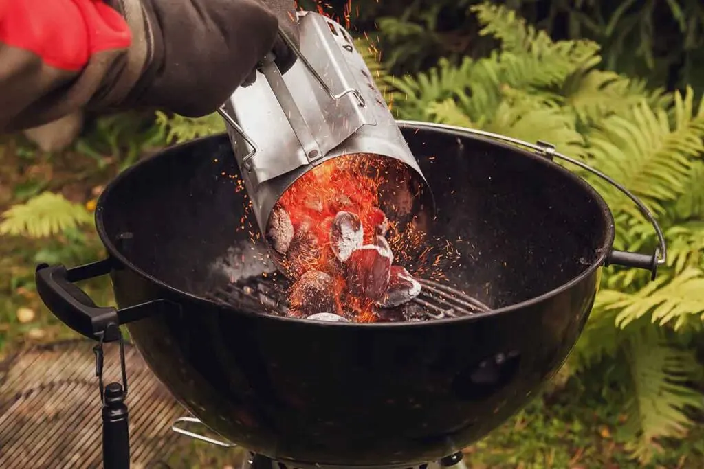 Hand dumping red hot charcoal from chimney starter.