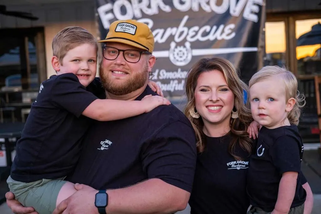 Dylan and Tiffani Cooke with their kids in front of sign hanging on their new restaurant, Fork Grove Barbecue.