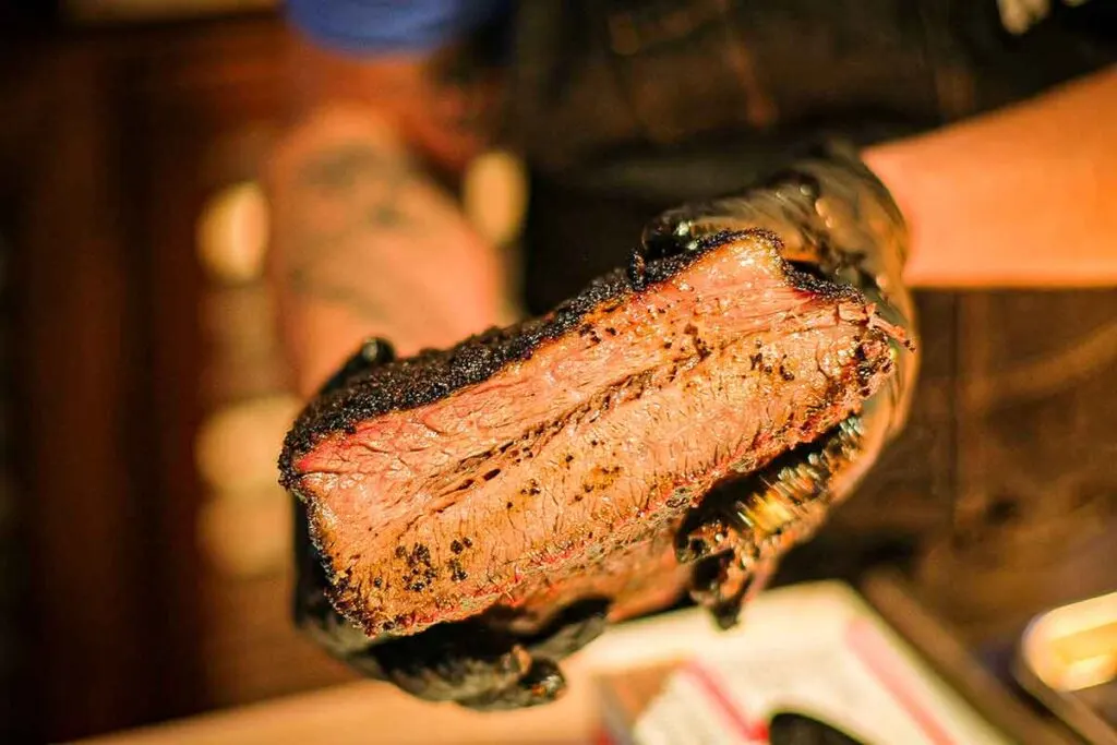 Two black-gloved hands holding a cross-section of juicy brisket.