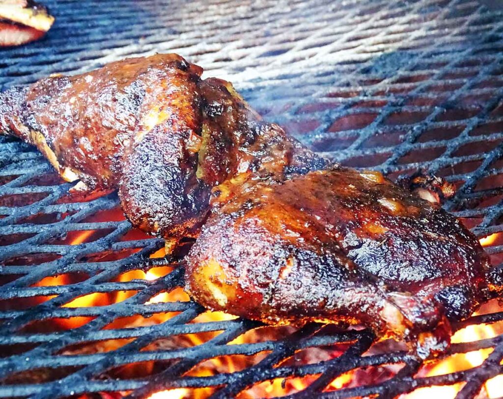 Two pieces of barbecued chicken on grill with glowing embers below the black grate.