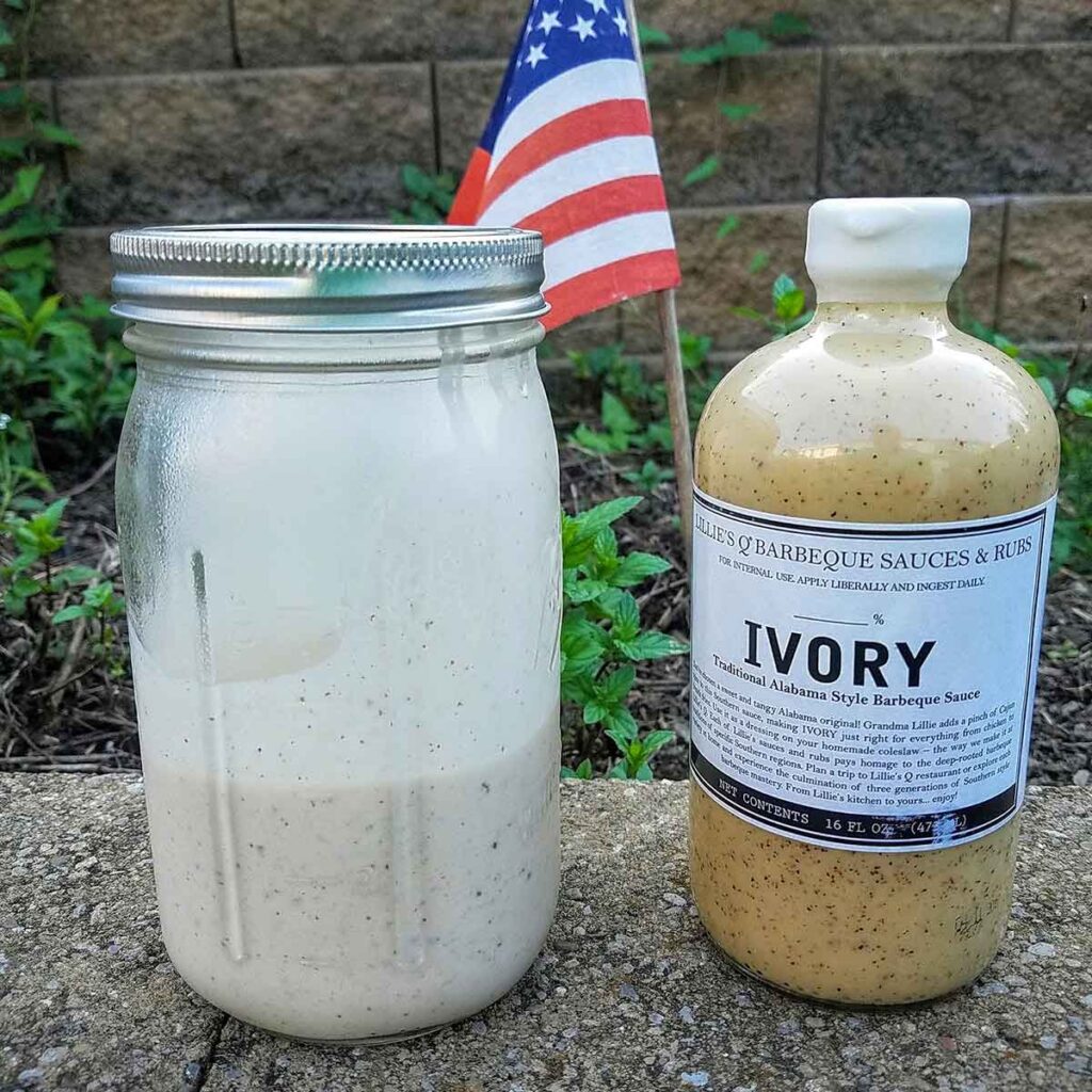 Homemade white sauce in quart sized mason jar beside bottle of store-bought Lille's Q Ivory sauce, which has a more yellow ting.