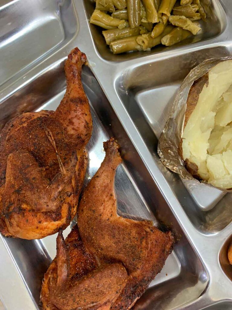 Metal tray with two smoked chicken halves and a baked potato.
