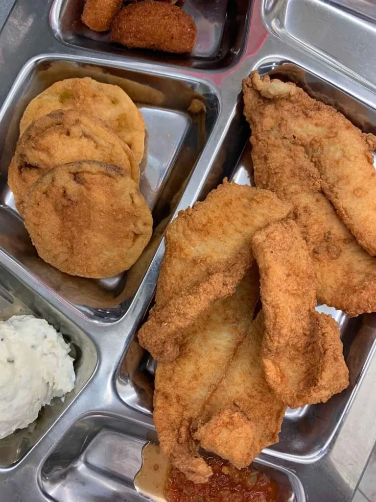 Silver metal tray with fried fish, fried green tomatoes and other sides.