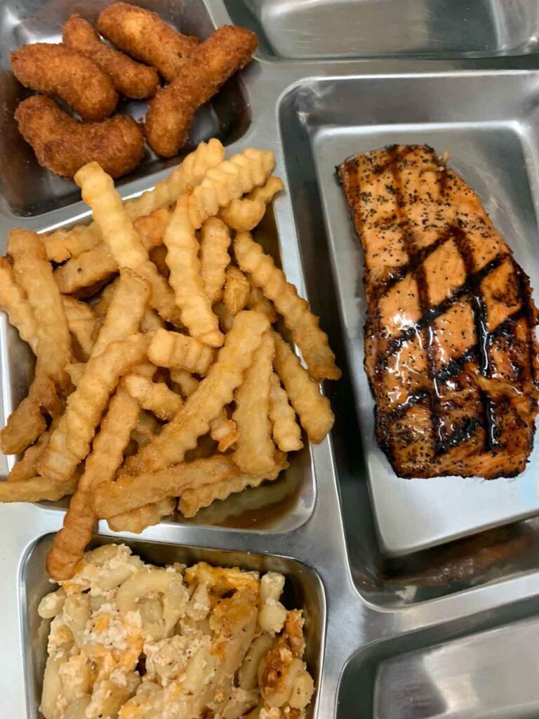 Glazed grilled salmon with fries and other sides.