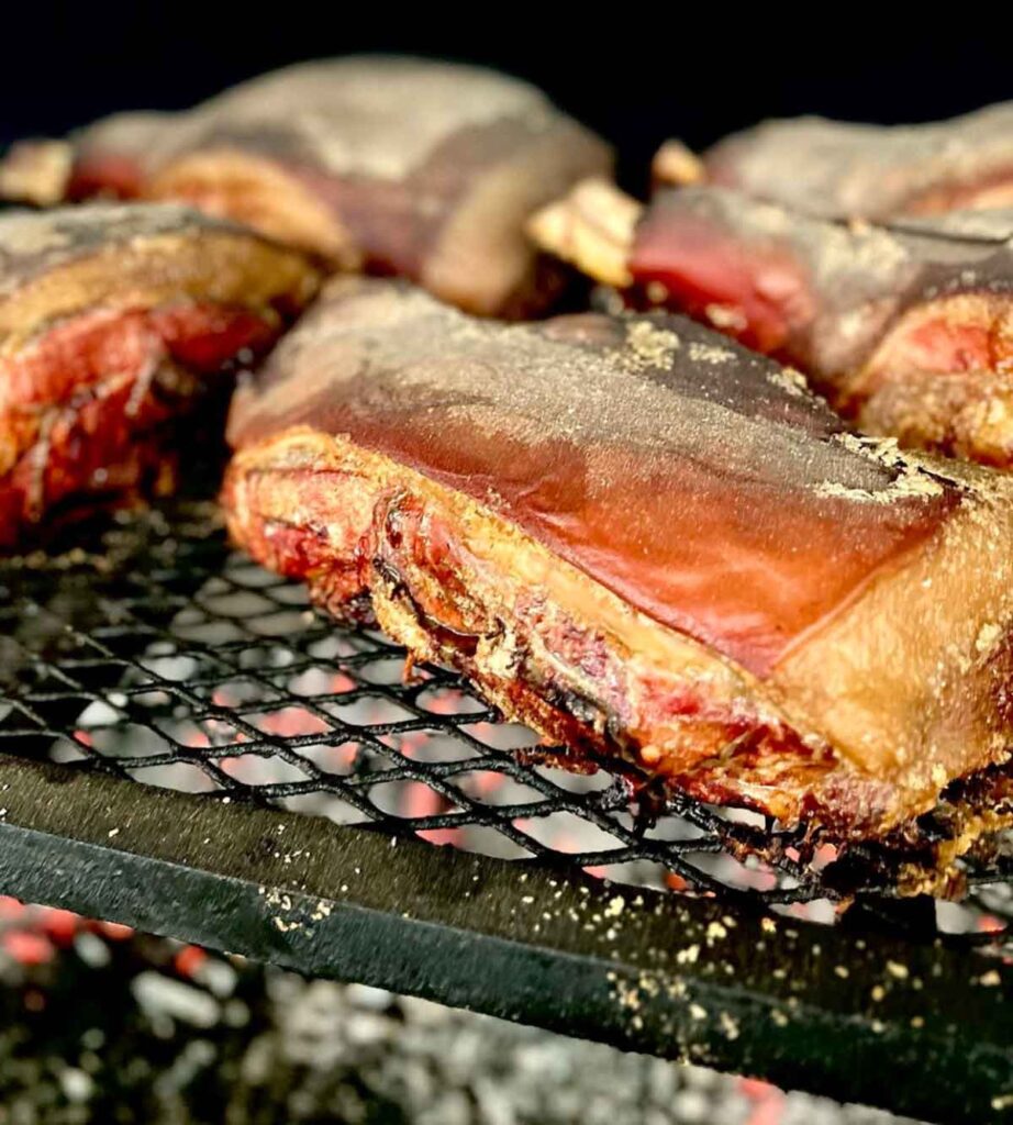 Pork shoulders on grill with embers below.