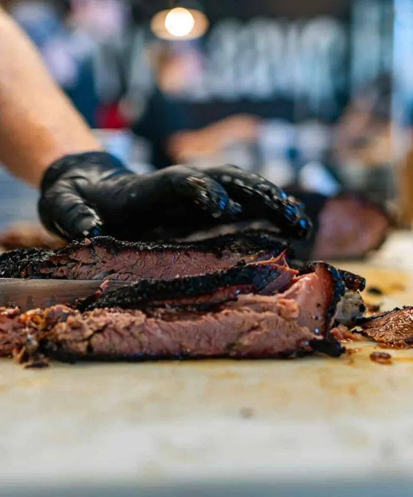 Hand holding down a brisket as it is sliced.
