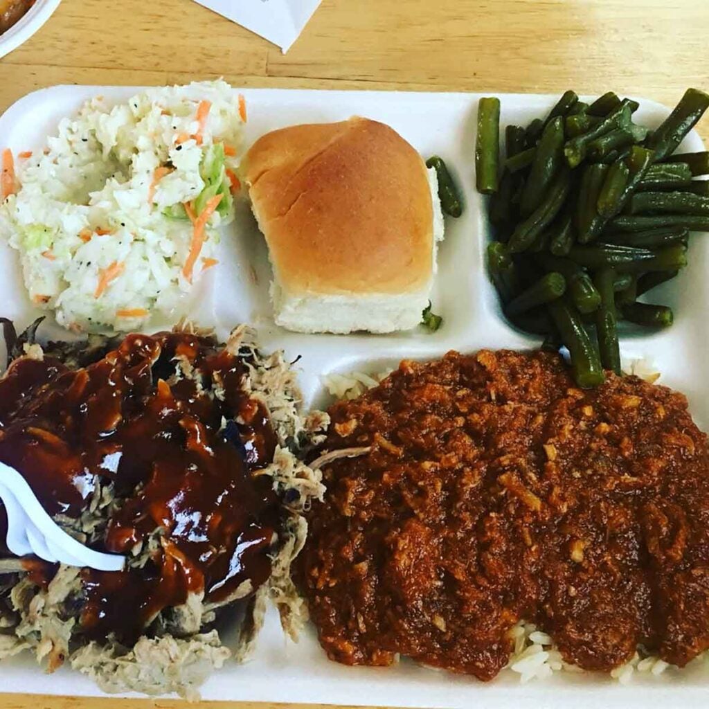Plate with sauced BBQ, hash and rice, slaw, green beans and a dinner roll.