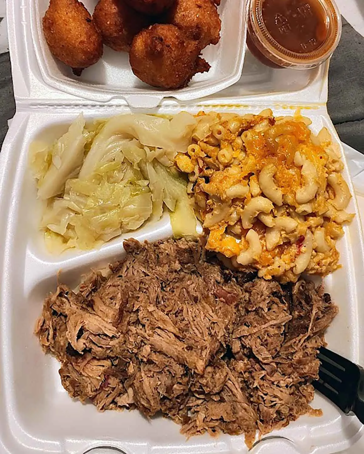 Styrofoam tray with bbq, mac and cheese, and stewed cabbage.