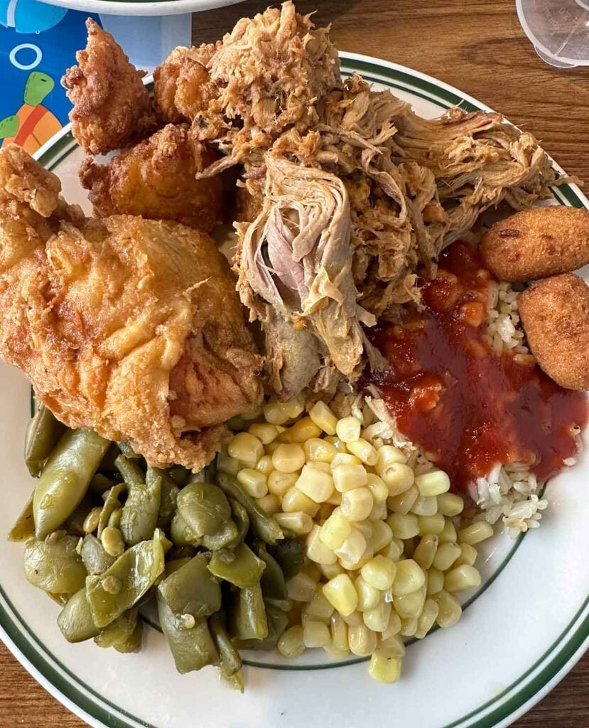 Overhead view of plate of BBQ, fried chicken, red gravy over rice, and sides.