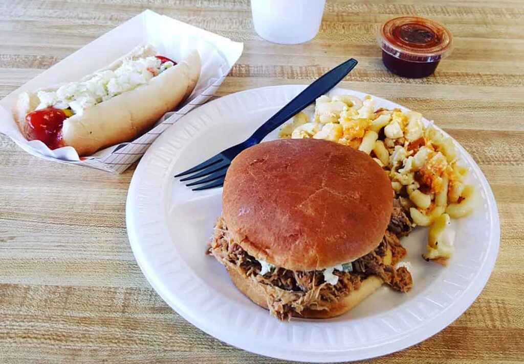 Plate with BBQ sandwich and slaw with hot dog in a tray on the side.