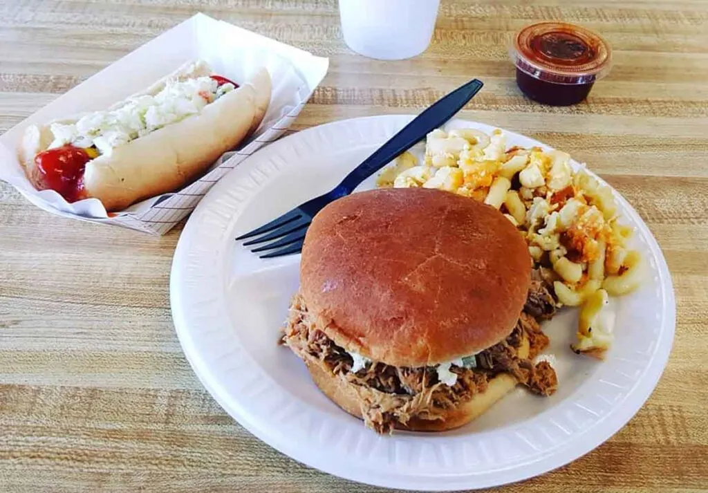 Plate with BBQ sandwich and slaw with hot dog in a tray on the side.