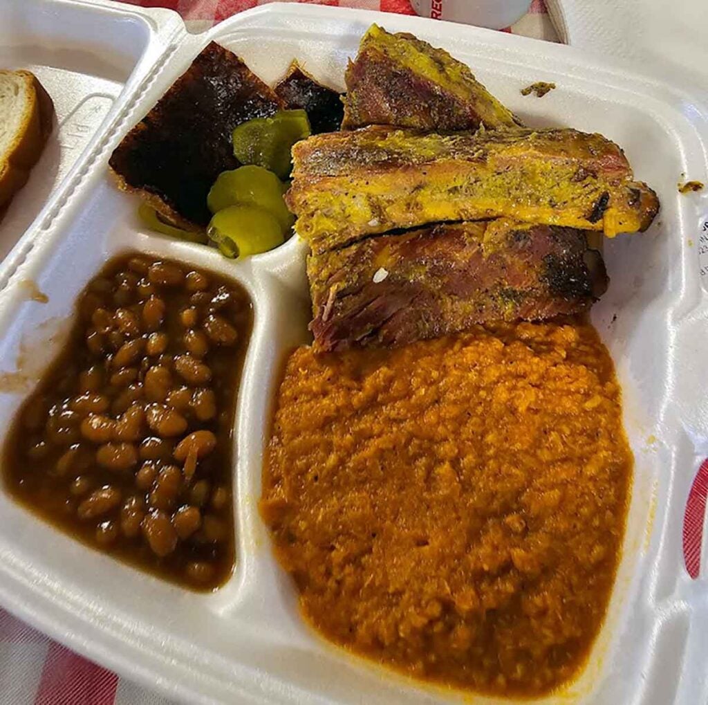 Styrofoam tray of hash and ribs with sides.