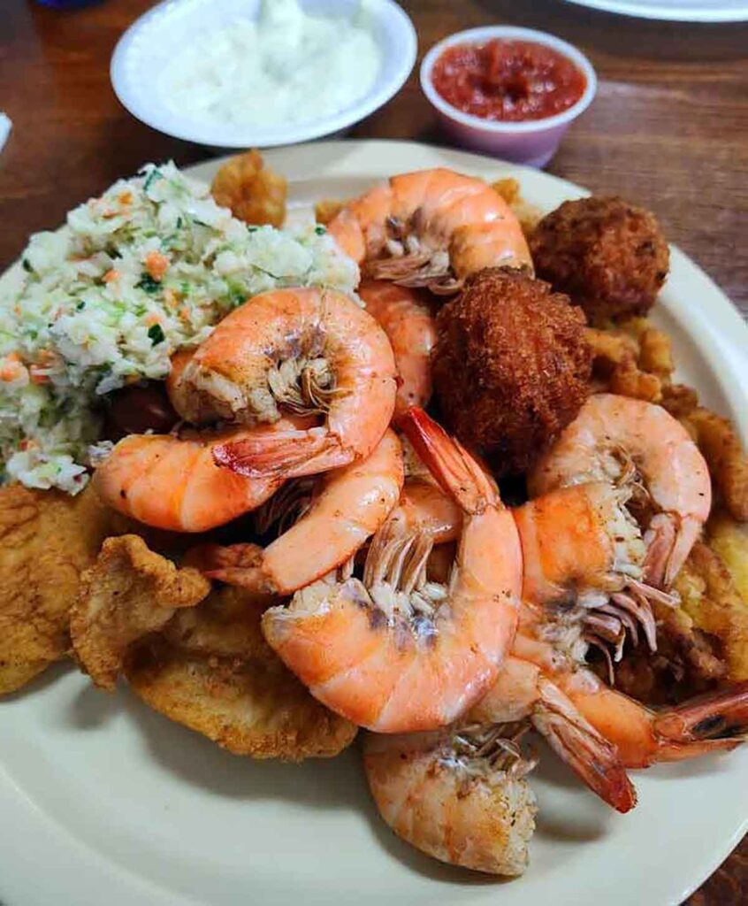 Plate piled with shrimp, hush puppies, slaw, and more.