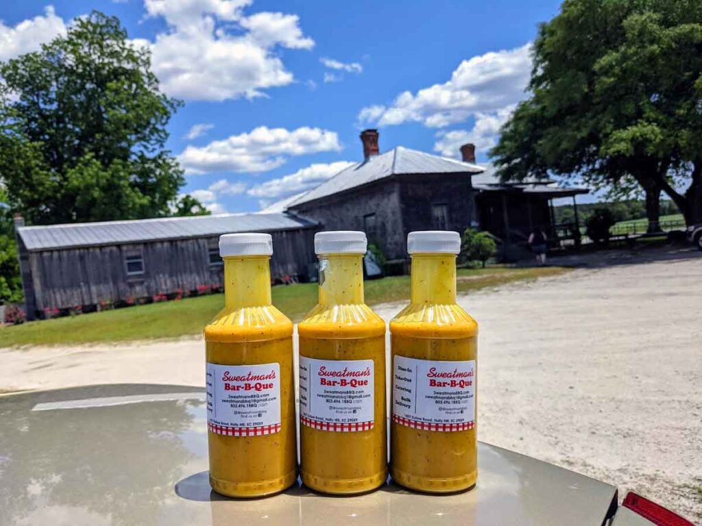 Three bottles of sauce on car with Sweatman's in background.