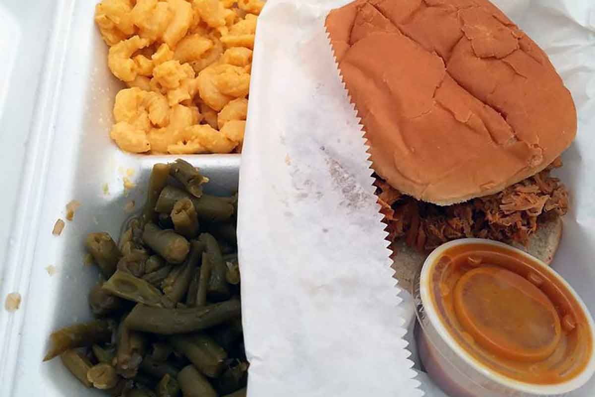 Takeout container of BBQ sandwich with sauce and sides from Big Ts.