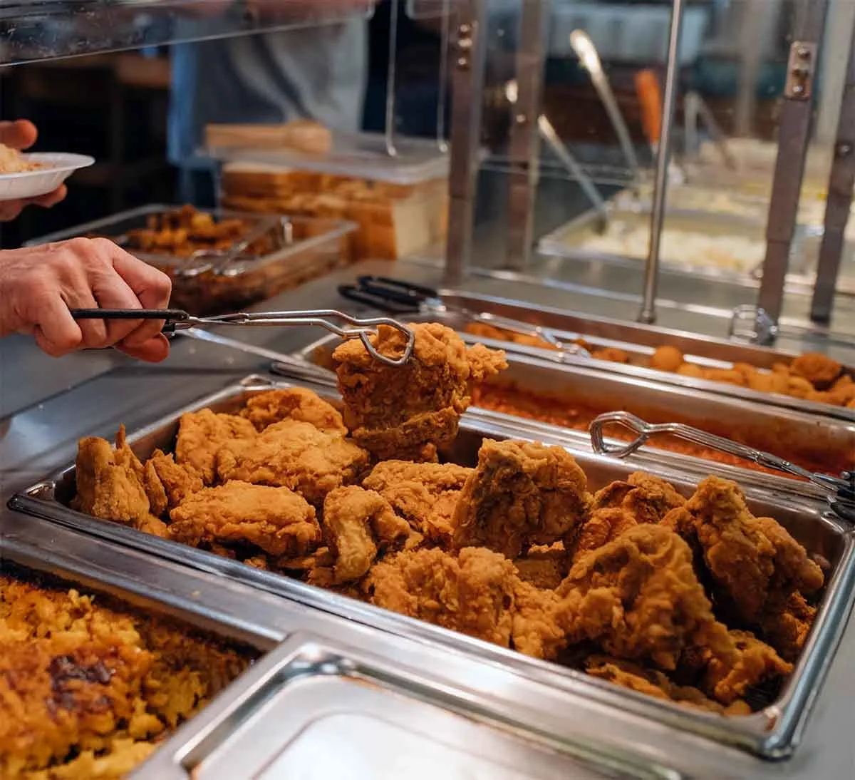 Someone picking up fried chicken from buffet with tongs.