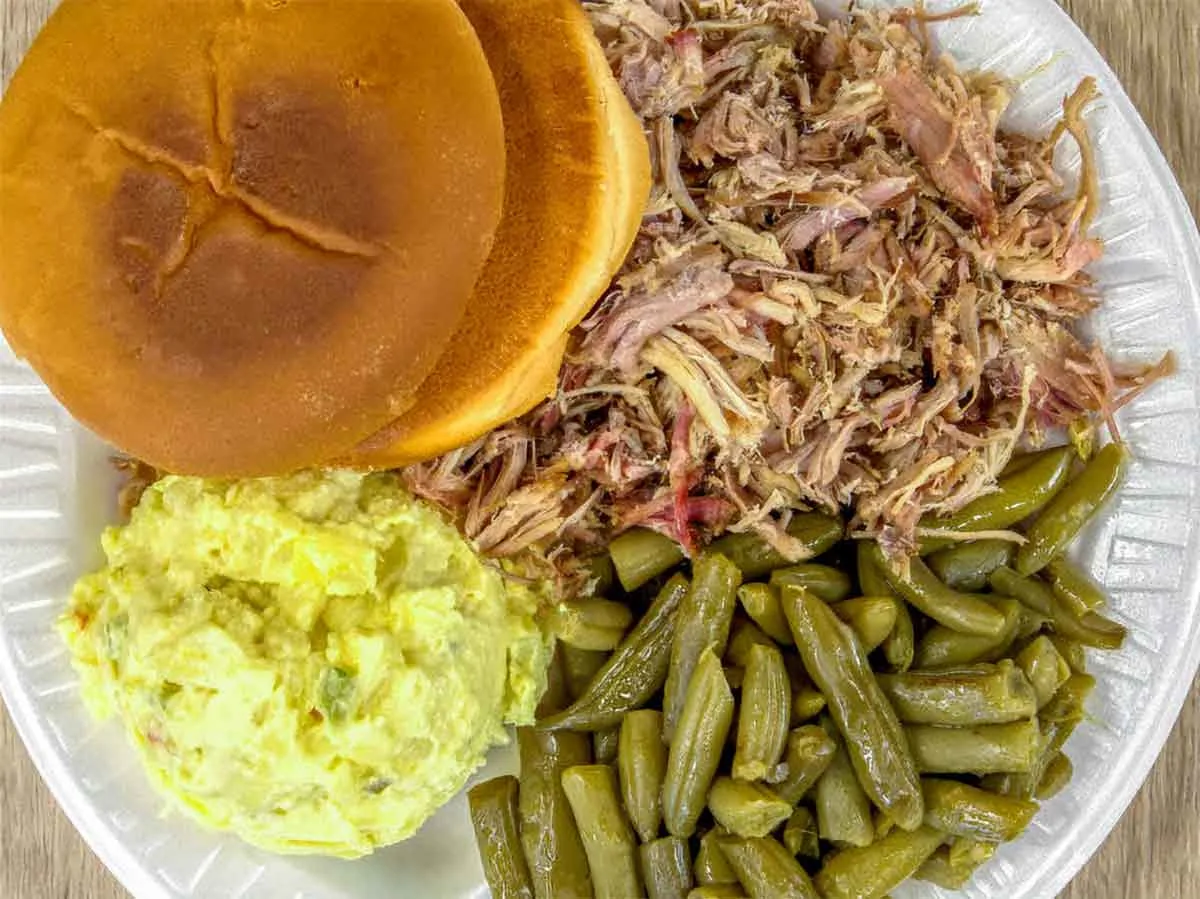 Pulled pork with bun, potato salad, and green beans.