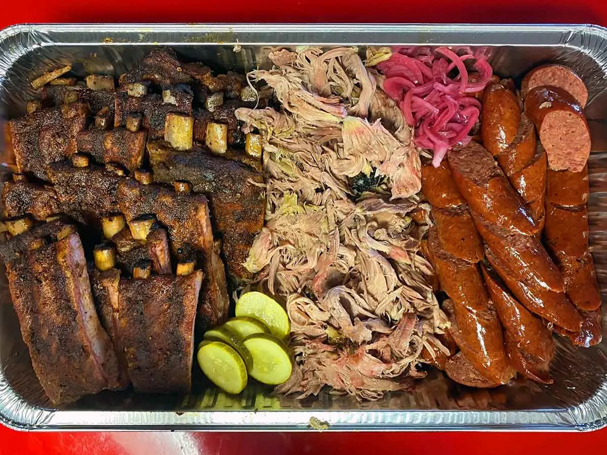 Catering tray with ribs, pulled pork, sausage and pickles.