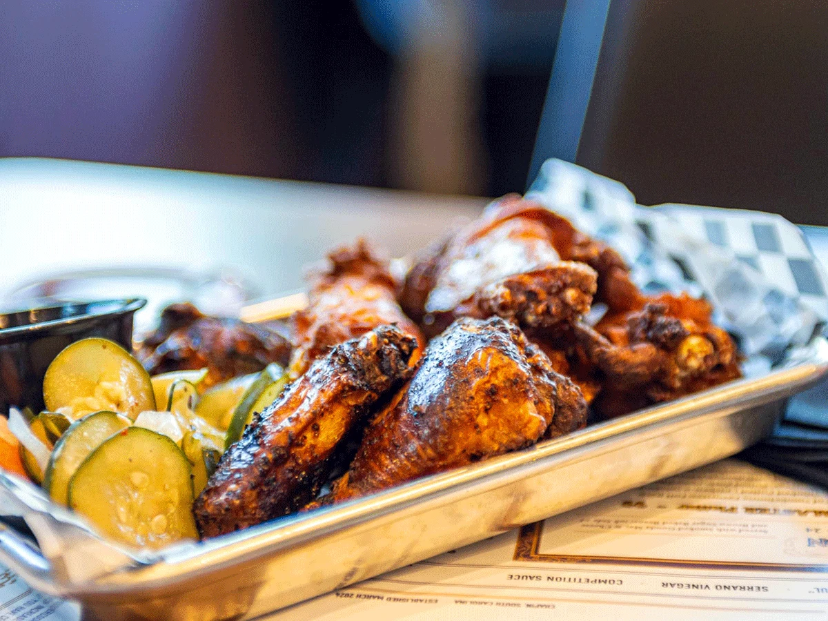 Smoked wings on metal serving tray with pickles.
