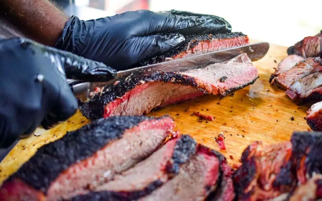 Hands slicing smoked brisket showing smoke ring.