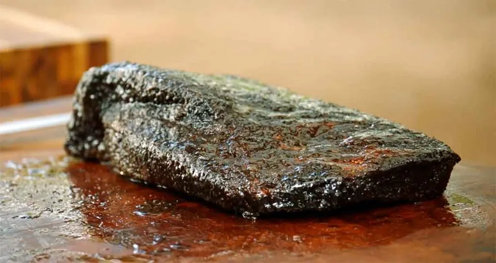Moist brisket sitting in juices on a cutting board outside.