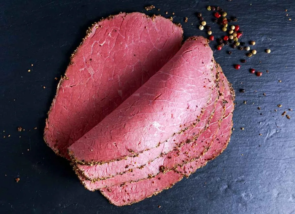 Peppered roast beef pastrami slices on paper with grains of coloured pepper.