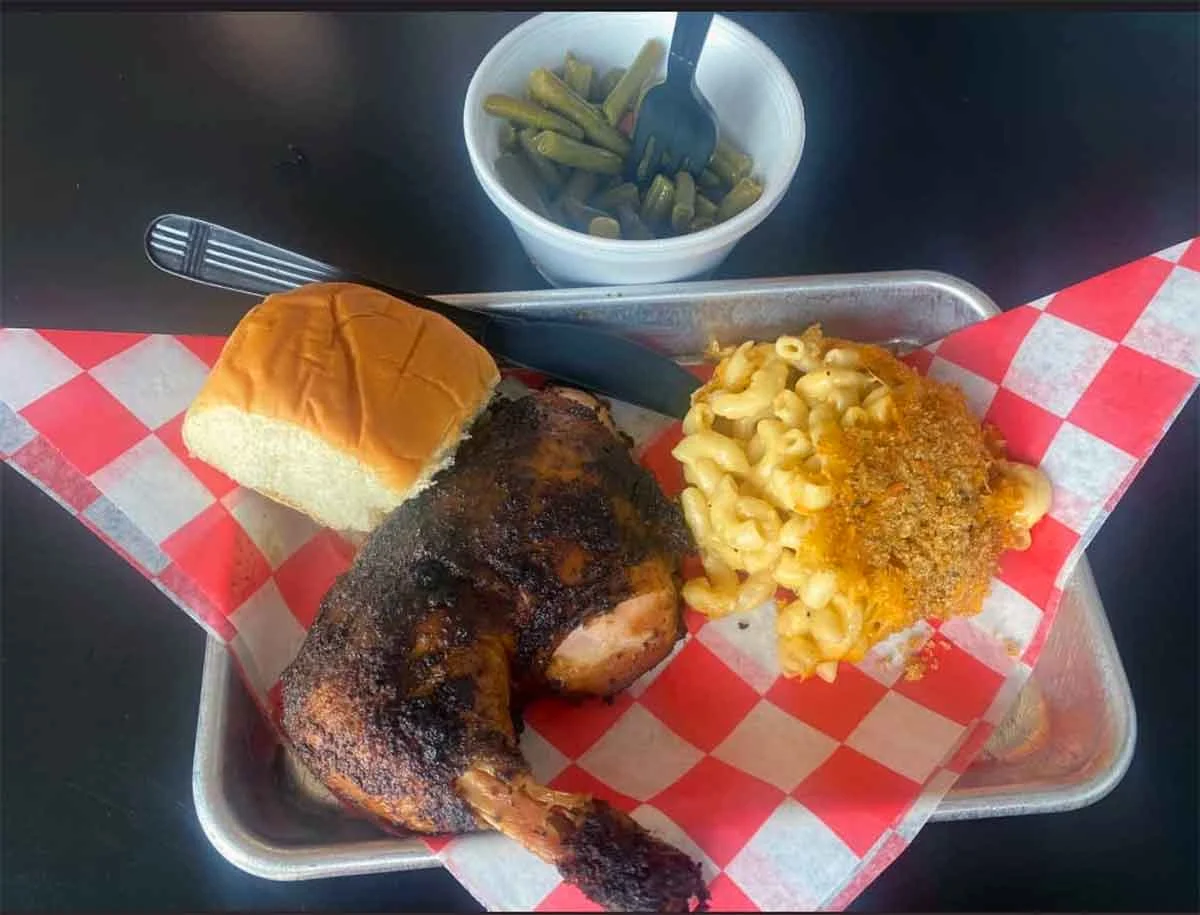 Smoked chicken quarter with sides of Mac and cheese and green beans with a dinner roll.