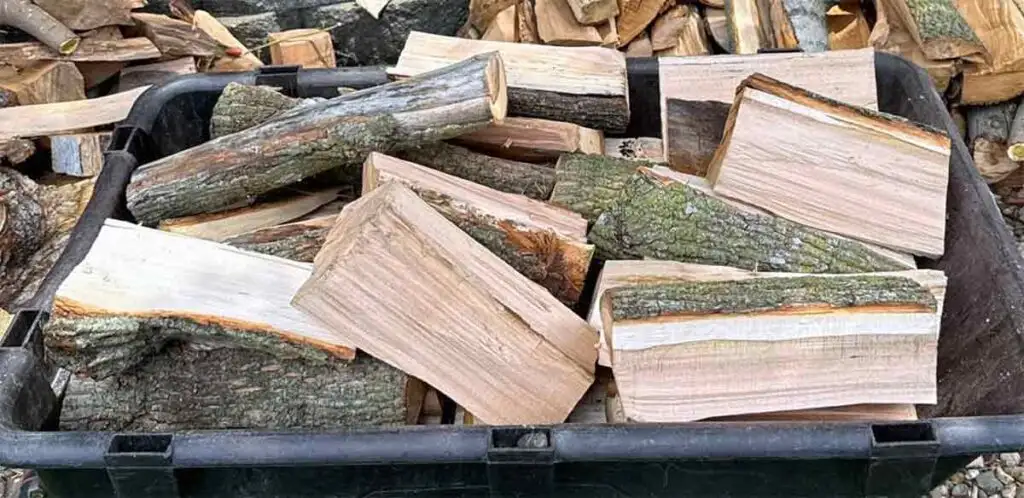 Maple wood splits in cart with stacked firewood in the background.